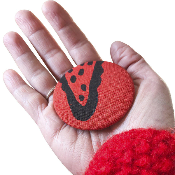 A hand holding a red 'Corn' magnet, bottle opener - Devrim Studio