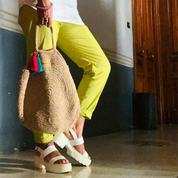 A young woman wearing a colorful outfit is holding her hemp handwoven handbag.
