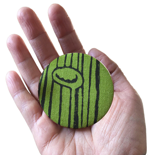 A hand holding a green 'Stuck to the floor' fridge magnet, bottle opener - Devrim Studio