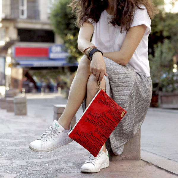 A woman holding a red 'Stuck to the Floor' iPad sleeve, clutch from it's wristlet - Devrim Studio